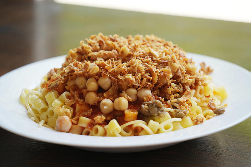 Koshari besteht aus Nudeln, Linsen, Kichererbsen, Tomatensoße und knusprigen Zwiebeln.