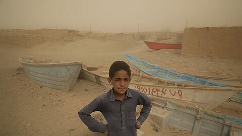 Ein Junge im Iran steht vor alten Booten, wo einst ein See war.
