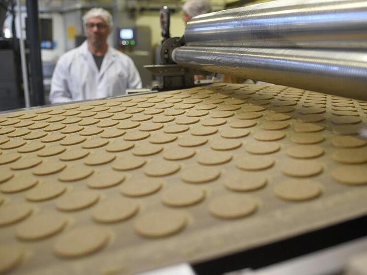 Kekse liegen bei einer Werksführung in der Printen-und Schokoladenfabrik Henry Lambertz GmbH & Co. KG auf einem Band. Die US-Strafzölle belasten auch die Deutsche Süßwarenindustrie.