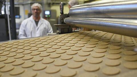 Kekse liegen bei einer Werksführung in der Printen-und Schokoladenfabrik Henry Lambertz GmbH & Co. KG auf einem Band. Die US-Strafzölle belasten auch die Deutsche Süßwarenindustrie.