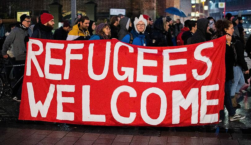 Teilnehmer einer Demonstration gegen die Verschärfung des Asylrechts halten in der Innenstadt in Hamburg ein Banner mit der Aufschrift "Refugees welcome".