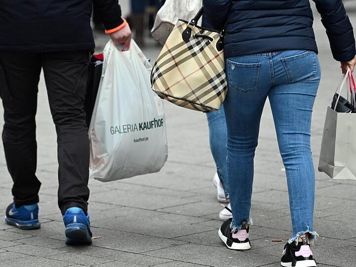 Menschen tragen in einer Einkaufsstraße Taschen und Tüten.