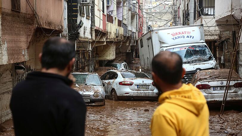 Menschen betrachten Fahrzeuge, die nach heftigen Regenfällen in Sanliurfa im Morast stehen.
