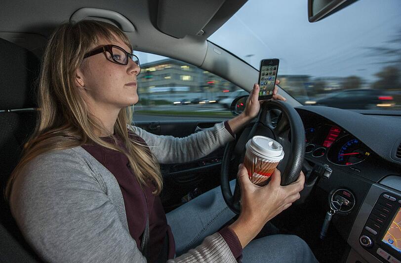 In einer Hand der Kaffee, in der anderen das Handy: Das sollten Autofahrer bleiben lassen.