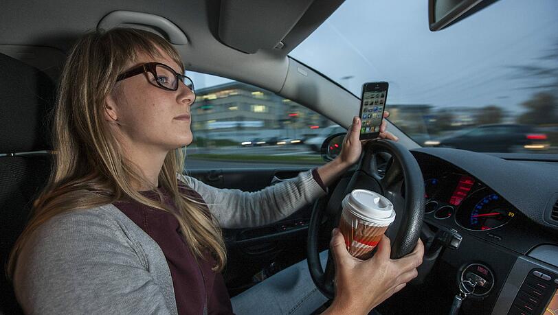 In einer Hand der Kaffee, in der anderen das Handy: Das sollten Autofahrer bleiben lassen. In einer Hand der Kaffee, in der anderen das Handy: Das sollten Autofahrer bleiben lassen.