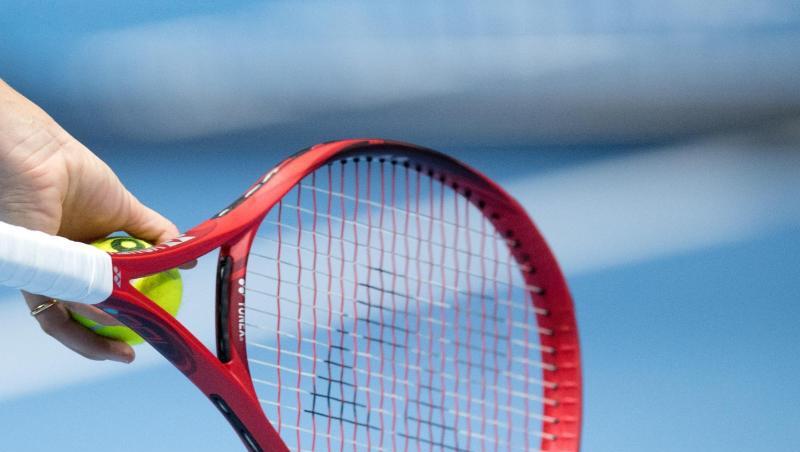 Eine Person hält einen Tennisschläger und einen Tennisball in der Hand.