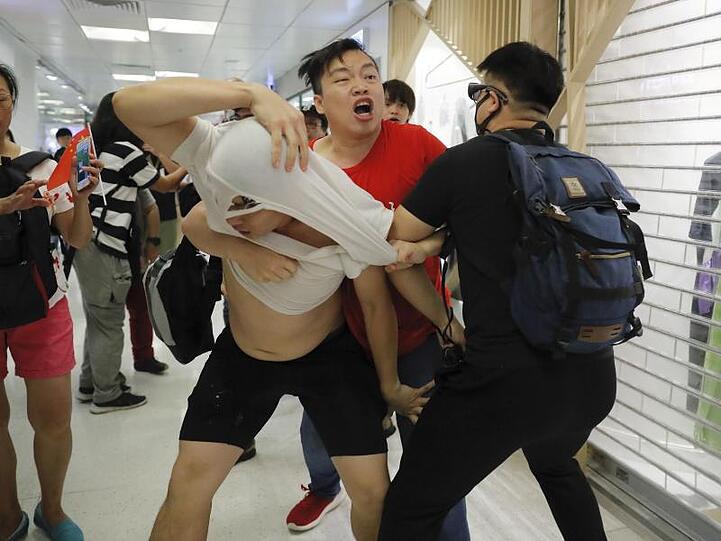 Ein Anhänger der Führung in Peking in einem roten T-Shirt und regierungskritische Demonstranten leisten sich handgreifliche Auseinandersetzungen.