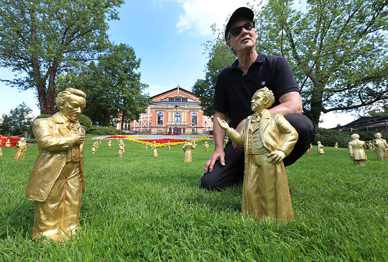 Der K&uuml;nstler Ottmar H&ouml;rl auf dem Gr&uuml;nen H&uuml;gel vor dem Festspielhaus, hinter zwei Skulpturen welche K&ouml;nig Ludwig II (rechts) und Richard Wagner darstellen. Die Skulpturen sind Teil einer Installation mit dem Titel &bdquo;Der M&auml;zen&ldquo;.