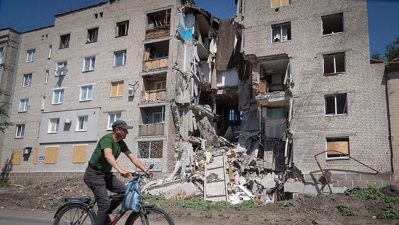 Bachmut: Ein Mann fährt mit dem Fahrrad an einem durch russischen Beschuss beschädigten Gebäude vorbei. Bachmut: Ein Mann fährt mit dem Fahrrad an einem durch russischen Beschuss beschädigten Gebäude vorbei.
