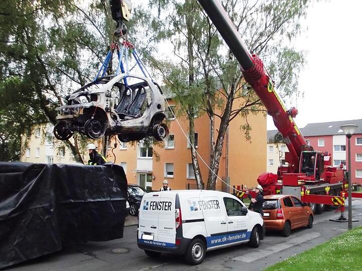 Ein Kranwagen der Dortmunder Feuerwehr hebt ein ausgebranntes E-Auto in einen Container.