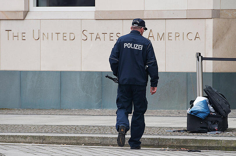 Ein Polizist begutachtet vor der US-Botschaft am Pariser Platz einen verdächtigen Koffer. Ein gewalttätiger Mann ist in Berlin festgenommen worden. Er hatte mit einem Bombenanschlag gedroht. Foto: Paul Zinken/Archiv