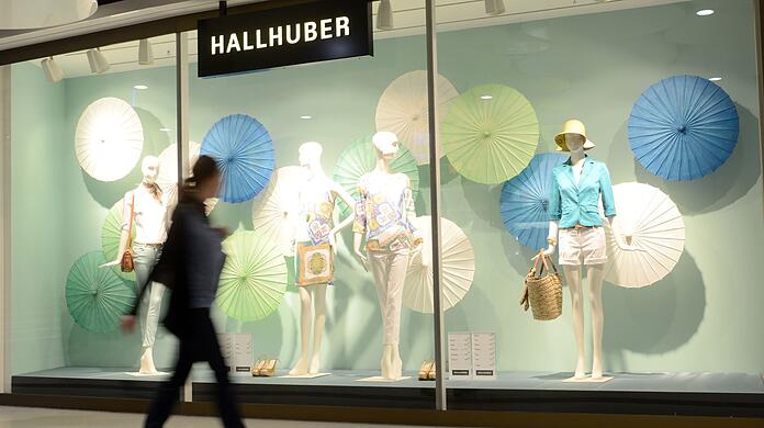 Eine Frau geht an einem Schaufenster des Modehauses Hallhuber vorbei.