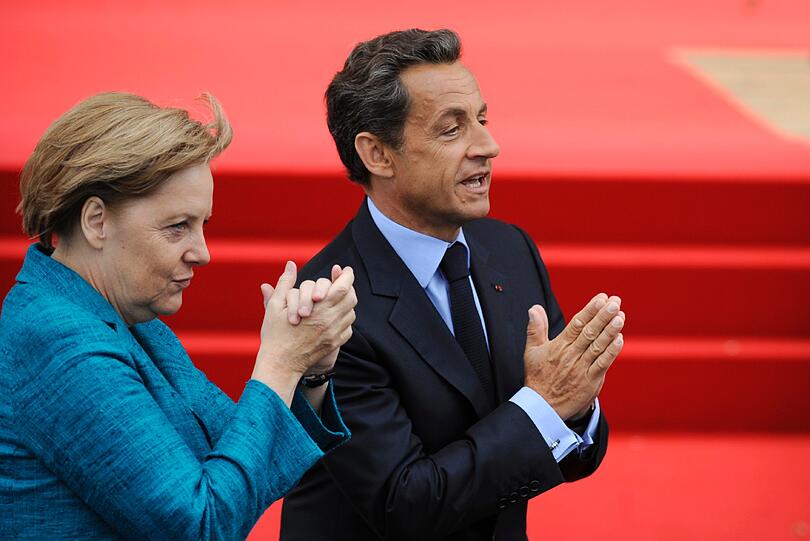 Die Kanzlerin und der Gastgeber: Angela Merkel und Nicolas Sarkozy grüßen in die Menge.