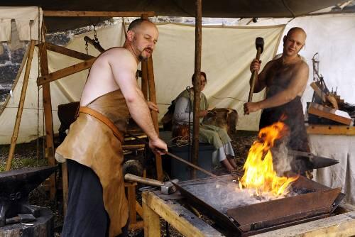 Gaukler, fahrende Leute und Handwerker lagern rund um die Burg. Hier zeigen zwei Schmiede ihre Kunst.