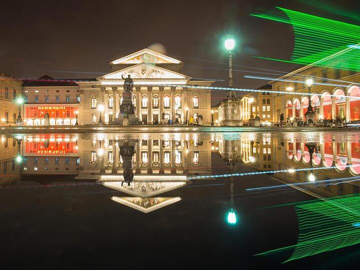 Die bayerische Staatsoper spiegelt sich in einer Pfütze auf der Residenzstraße. Foto: Peter Kneffel/Archiv