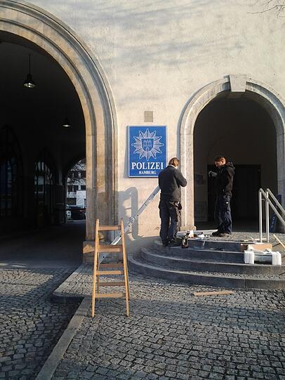 Zwei Filmcrew-Mitglieder vor dem "Polizei Hamburg"-Schild in der Anzinger Straße.