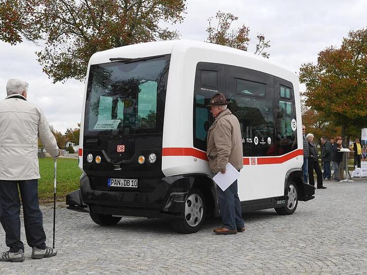 Zwei Männer betrachten einen autonom fahrenden Minibus auf einer Straße in Bad Birnbach. Foto: Tobias Hase/dpa