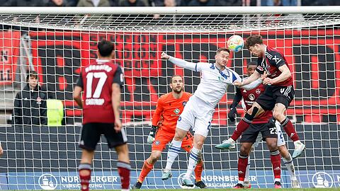 Nürnberger James Lawrence (r) liefert sich mit Karlsruhes Christoph Kobald (M) ein Kopfballduell.
