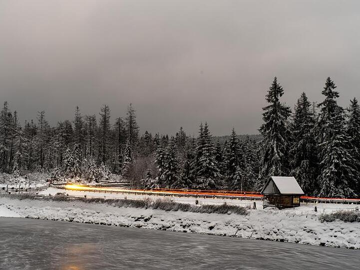 Lichtspuren von vorbeifahrenden Autos sind vor der schneebedeckten Landschaft am Oderteich im Harz zu sehen. Es kann glatt werden auf den Straßen.