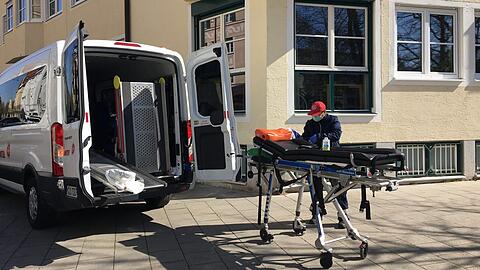 Ein Krankentransportfahrer desinfiziert die Liege, auf der eine Heimbewohnerin lag. Hinter den dunklen Scheiben schaut ihm eine andere Bewohnerin dabei zu.