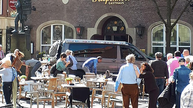 Menschen stehen vor einem der Lokale am Kiepenkerl in Münster, kurz nachdem ein Fahrzeug in das Straßencafe gefahren war.