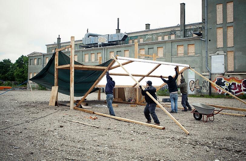 Die für ihre provokanten Videoinstallationen und Live-Performances bekannte Münchner Künstlerin Funda bespielt einen dezentralen Ort der Stadt: den Bereich zwischen Jutier- und Tonnenhalle in der Dachauer Straße 110. Ihr Projekt hematisiert das Verweilen an einem unscheinbaren Ort, einem "Nicht-Ort" in Zeiten". Das Foto zeigt den Aufbau.