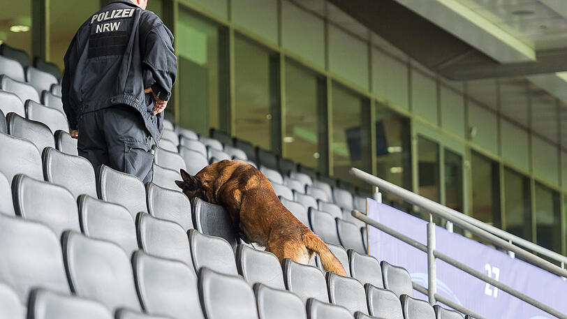 Ein Polizeibeamter durchsucht mit seinem Sprengstoff-Spürhund die Sitzreihen auf der Haupttribüne im Signal-Iduna-Park in Dortmund.