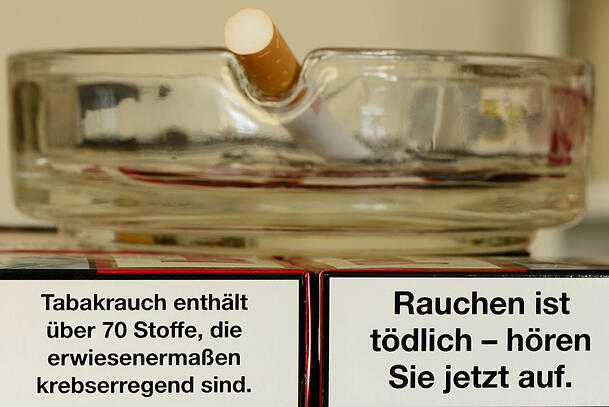 Auf zwei Zigarettenpackungen mit Gesundheitswarnung steht ein Aschenbecher.