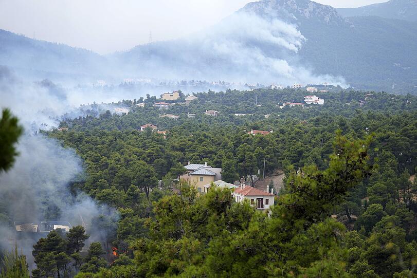 Rauch steigt während der Waldbrände aus einem Waldgebiet um eine Ortschaft empor. Starke Westwinde fachten die Waldbrände in der Region weiter an. Nördlich von Athen wurden die Menschen mehrerer Ortschaften aufgerufen, die Region zu verlassen.