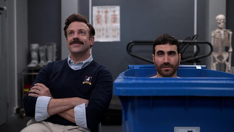 Ted Lasso (Jason Sudeikis) bearbeitet seinen grummelnden, in der Eistonne sitzenden Football-Kapitän Roy Kent (Brett Goldstein).
