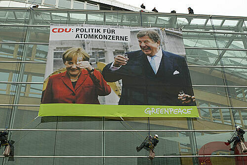 Prost! Zwölf Greenpeace-Aktivisten haben ein denkwürdiges Schnapsglas-Foto mit Kanzlerin und RWE-Chef am Adenauer-Haus aufgehängt. Die CDU zeigte die Aktivisten an.