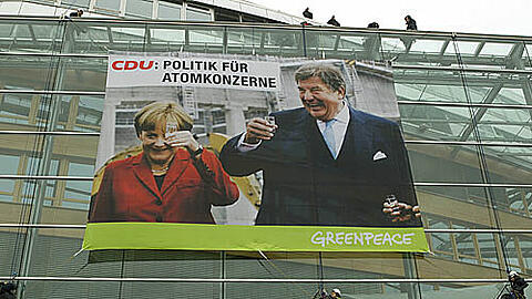 Prost! Zwölf Greenpeace-Aktivisten haben ein denkwürdiges Schnapsglas-Foto mit Kanzlerin und RWE-Chef am Adenauer-Haus aufgehängt. Die CDU zeigte die Aktivisten an.