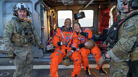 Die Astronauten Victor Glover und Christina Koch sitzen auf einem Hubschrauber der Navy auf dem Flugdeck des Schiffs USS John P. Murtha, nachdem sie aus ihrem "Orion"-Raumschiff geholt wurden.