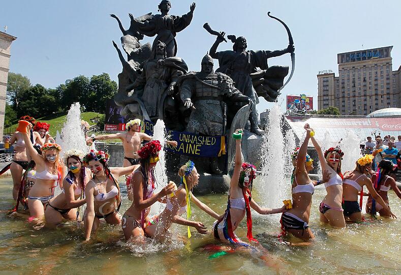 In weißen durchsichtigen Bikinis plantschen sie im Brunnen. Aber wieso?