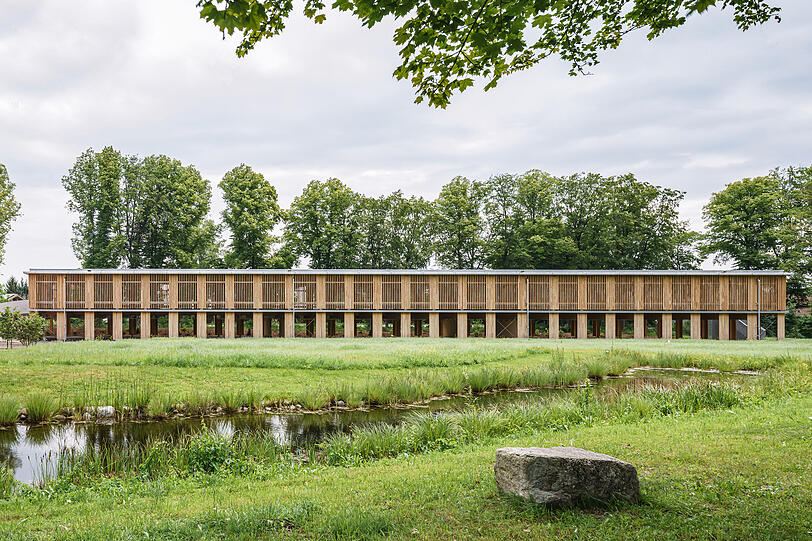 Das langgestreckte, offene Holzparkdeck soll sich mit seiner natürlichen Holzlamellen-Fassade in die umgebende Naturlandschaft einfügen. Das langgestreckte, offene Holzparkdeck soll sich mit seiner natürlichen Holzlamellen-Fassade in die umgebende Naturlandschaft einfügen.