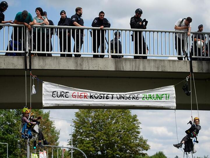 Zwei Kinder haben sich von einer Brücke abgeseilt und entfalten ein Transparent.