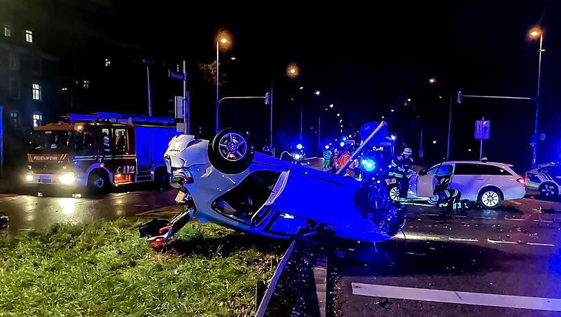 Einsatzkräfte befreien den eingeklemmten BMW-Fahrer aus dem auf dem Dach liegenden Fahrzeug an der Kreuzung Dietlindenstraße/Biedersteiner Straße.
