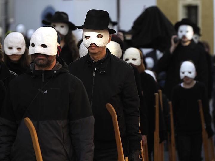 Teilnehmer einer Osterprozession gehen in schwarzen Gewändern und weißen Masken durch die Straßen von Budweis in Tschechien.