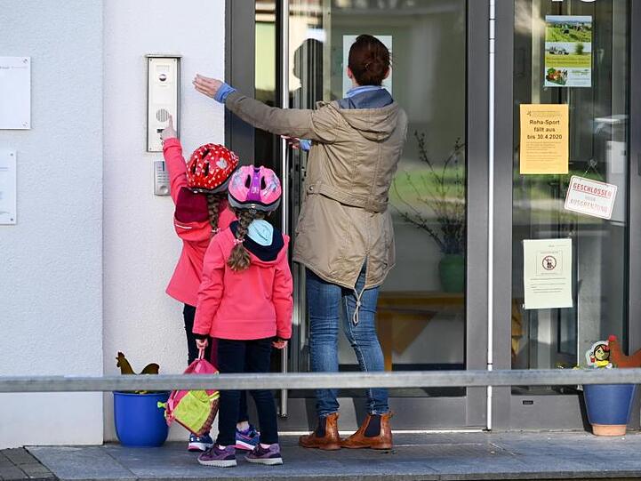 Eine Mutter steht mit ihren Kindern vor dem Kita-Eingang und klingelt.