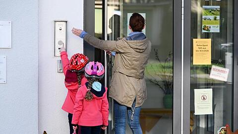 Eine Mutter steht mit ihren Kindern vor dem Kita-Eingang und klingelt.