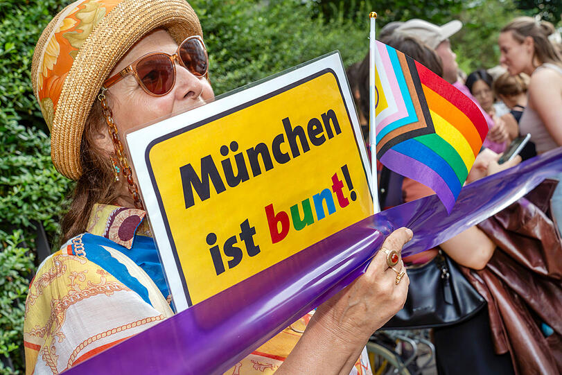 Queere Demo mit Menschenkette:Teilnehmerin mit Schild München ist bunt und Regenbogenfahne