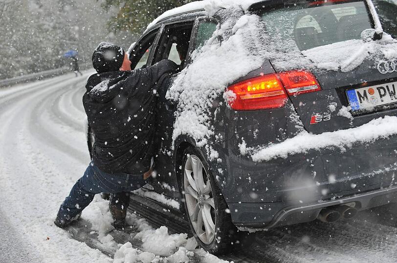 Ein Mann versucht am Samstag auf der Straße von Spitzingsee nach Schliersee (Oberbayern) ein Auto abzubremsen, das im Schnee den Berg hinunterfährt und dabei rutscht.