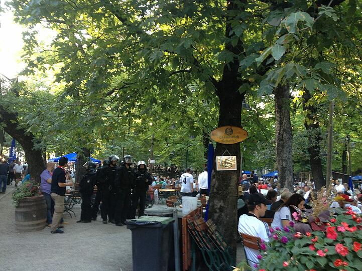 USK-Beamte (in dunkelblauen Overalls) stürmen in den Biergarten, um die Raufbolde zu trennen.