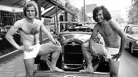 In Badehosen stehen die beiden damaligen Fußballer des FC Bayern München, Uli Hoeneß (l) und Paul Breitner vor einem Oldtimer.
