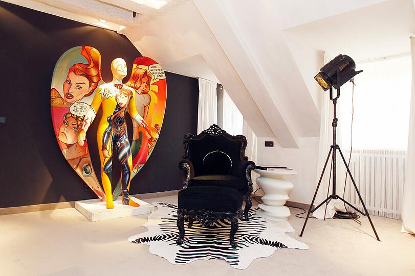 Pop-Art a la Gottschalks: Der Comic-Engel steht vor dem schwarzen Thron-artigen Stuhl, ein Scheinwerfer dient als Lampe.