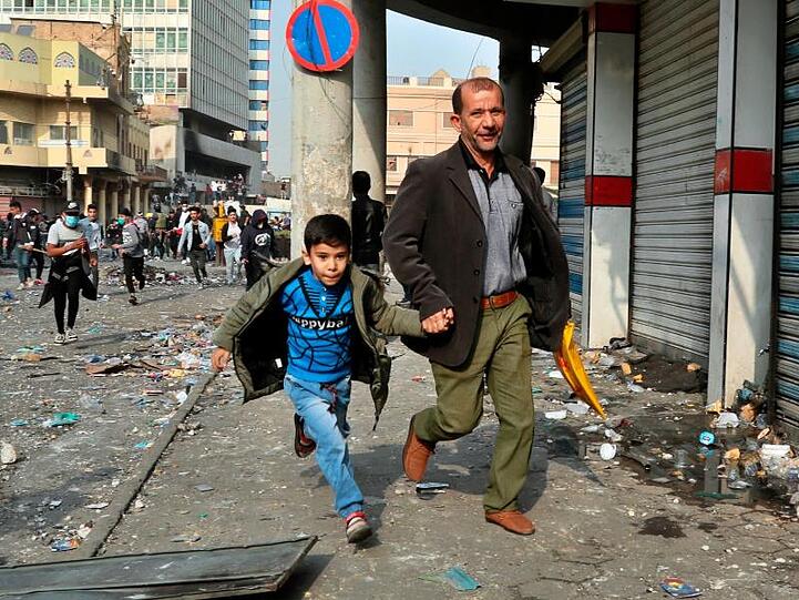 Ein Mann und sein Sohn flüchten vor Zusammenstößen zwischen irakischen Sicherheitskräften und regierungskritischen Demonstranten in Bagdad.