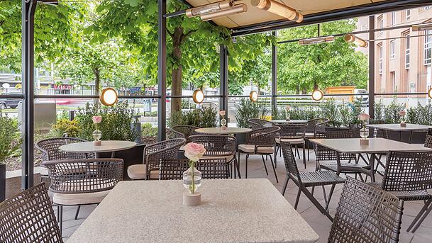 Bei sch&ouml;nem Wetter k&ouml;nnen die G&auml;ste auch drau&szlig;en sitzen. Die trubelige Rosenheimer Stra&szlig;e wird mit vielen Pflanzen abgeschirmt.