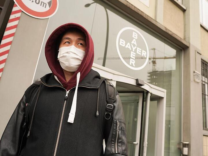 Ein Mann mit Mundschutz geht an einem Logo des Chemiekonzerns Bayer vorbei.