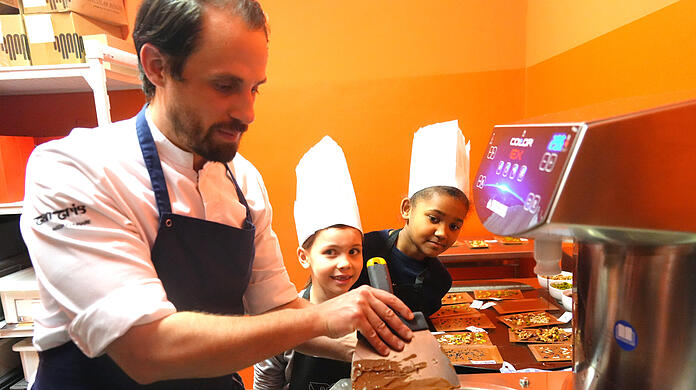 Wer an der Schokoladen- Quelle steht, bekommt die ganze Aufmerksamkeit. Chef-Patissier Maxime Rebmann zeigt den Schülern, wie aus der flüssigen Schokolade eine knackige Tafel wird. Das dürfen die Kinder natürlich auch selbst ausprobieren und ihre Tafeln anschließend mit Pistazien, Mandeln und mehr bestücken.