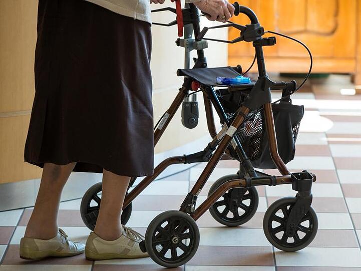 Eine Seniorin geht mit einer Gehhilfe über einen Flur. Foto: Daniel Karmann/dpa/Symbolbild